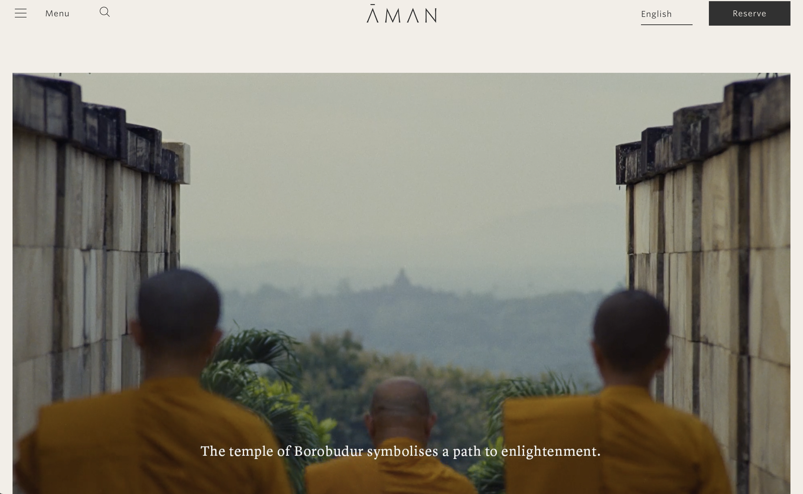 Aman luxury hotel homepage hero banner, three Buddhist monks in yellow robes viewing misty Borobudur temple, minimalist site navigation, cultural wellness travel imagery with Borobudur enlightenment quote overlay