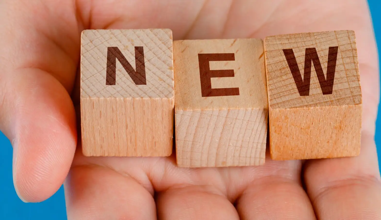 A hand holds wooden cubes with the word "new"