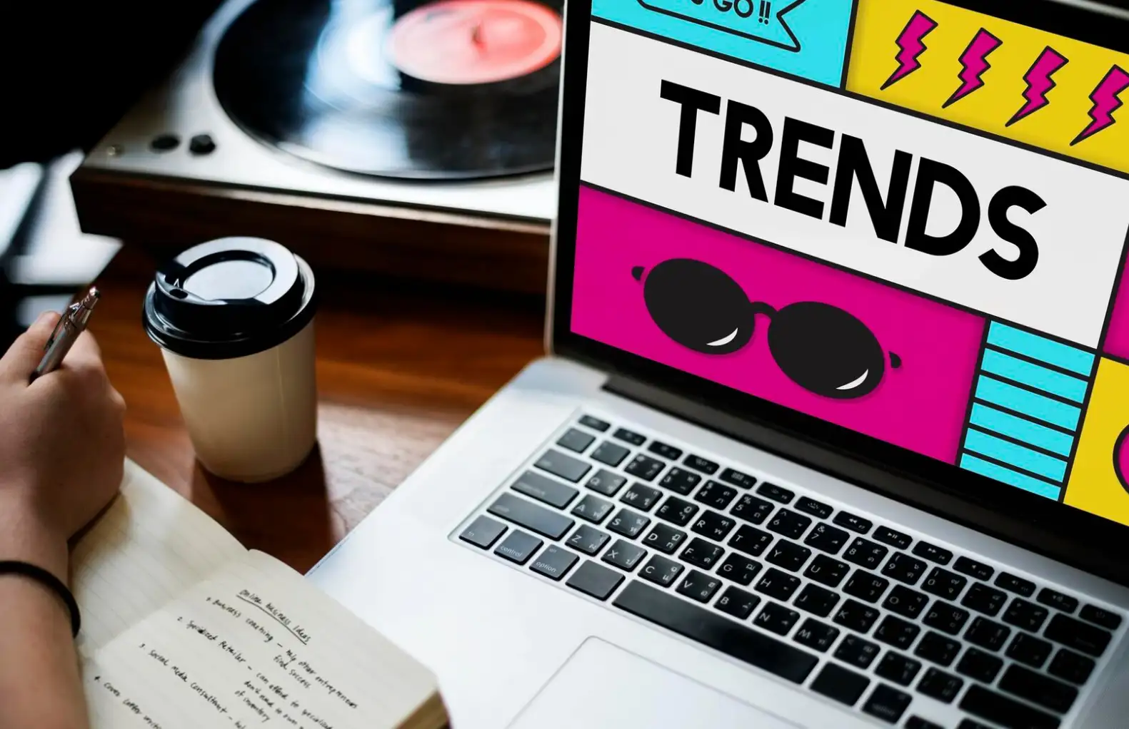 Writing in a notebook and watching trends on a laptop