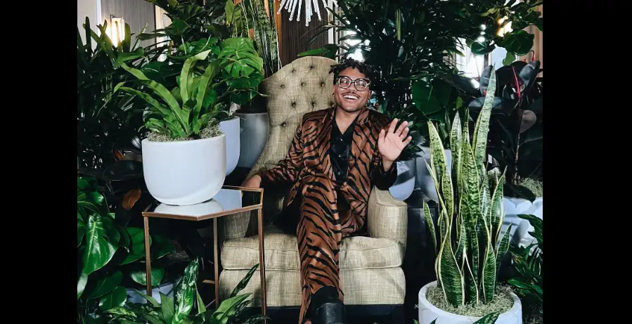 A man wearing a tiger-patterned suit sat on a sofa surrounded by potted plants.