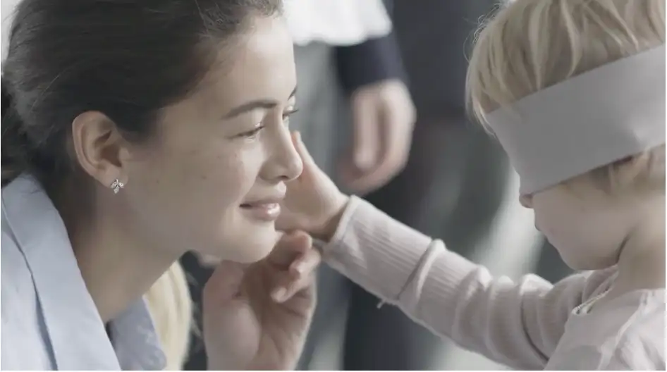 A blindfolded child is caressing its mother's cheek