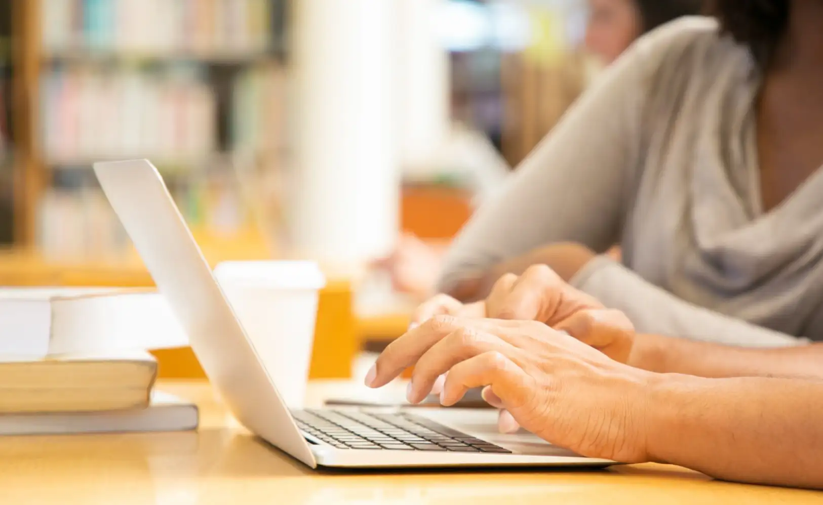 woman's hands typing on a laptop in a library