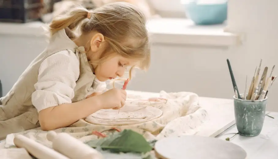 a little girl making a clay plate and decorating it