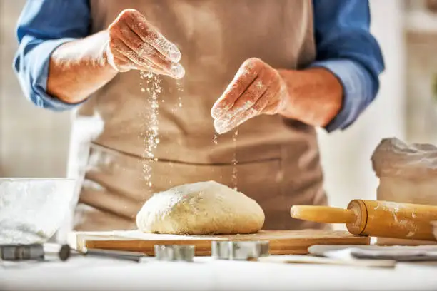 person dusting flour over dough with rolling pin nearby